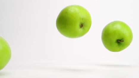 Whole-green-Granny-Smith-apples-falling-onto-white-table-top-and-bouncing-off-of-each-other-in-slow-motion