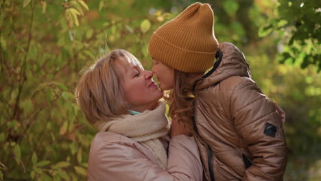 lovely moment with mother and daughter nestled in sunlit autumn woods, mom gently hugging child while golden light filters through colourful leaves, faces glowing with warmth and joy