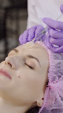 A beautiful woman is on the procedure of facial rejuvenation. Beautician makes mesotherapy of the forehead area. Beauty injections Vertical video