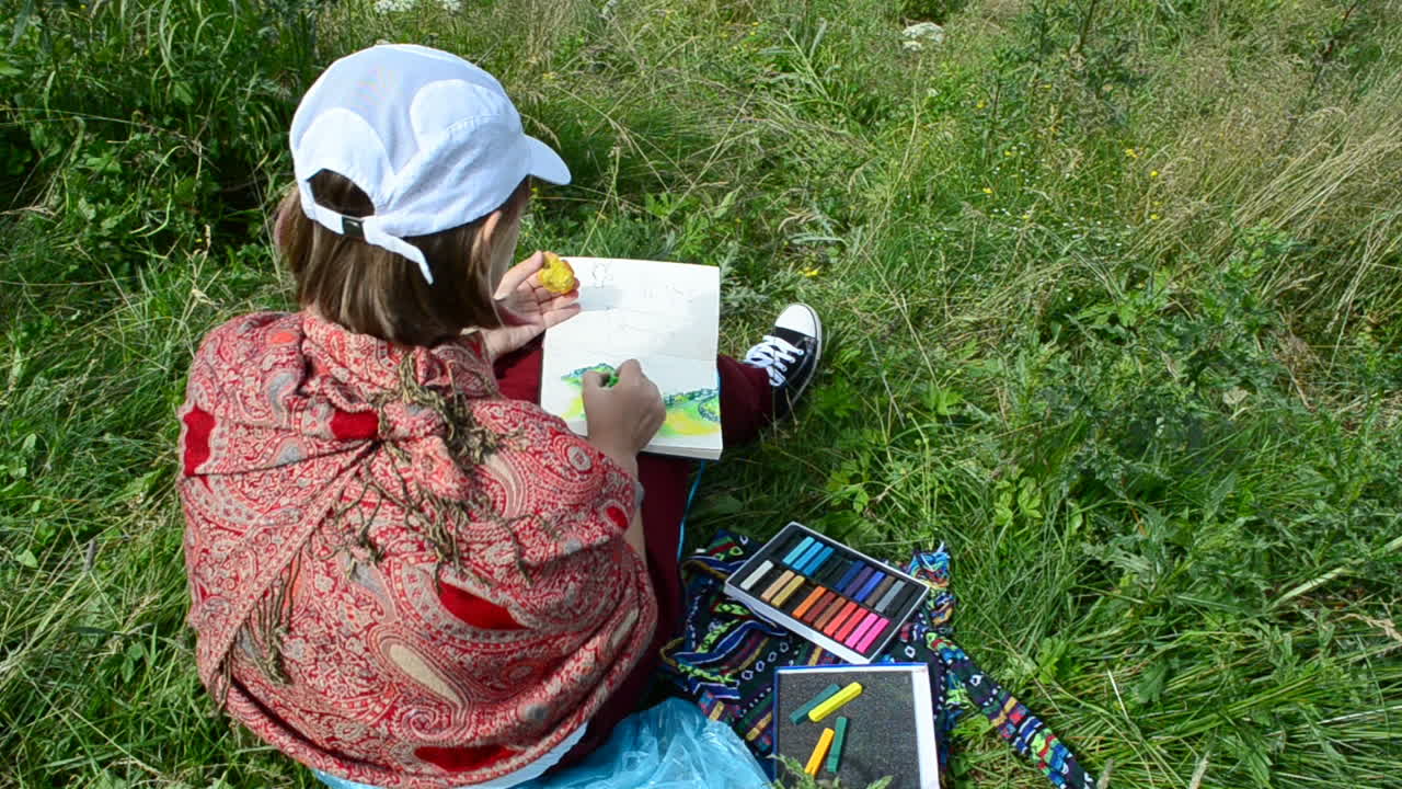 La ragazza disegna un paesaggio montano dal vero. Il disegno è realizzato con un pastello
