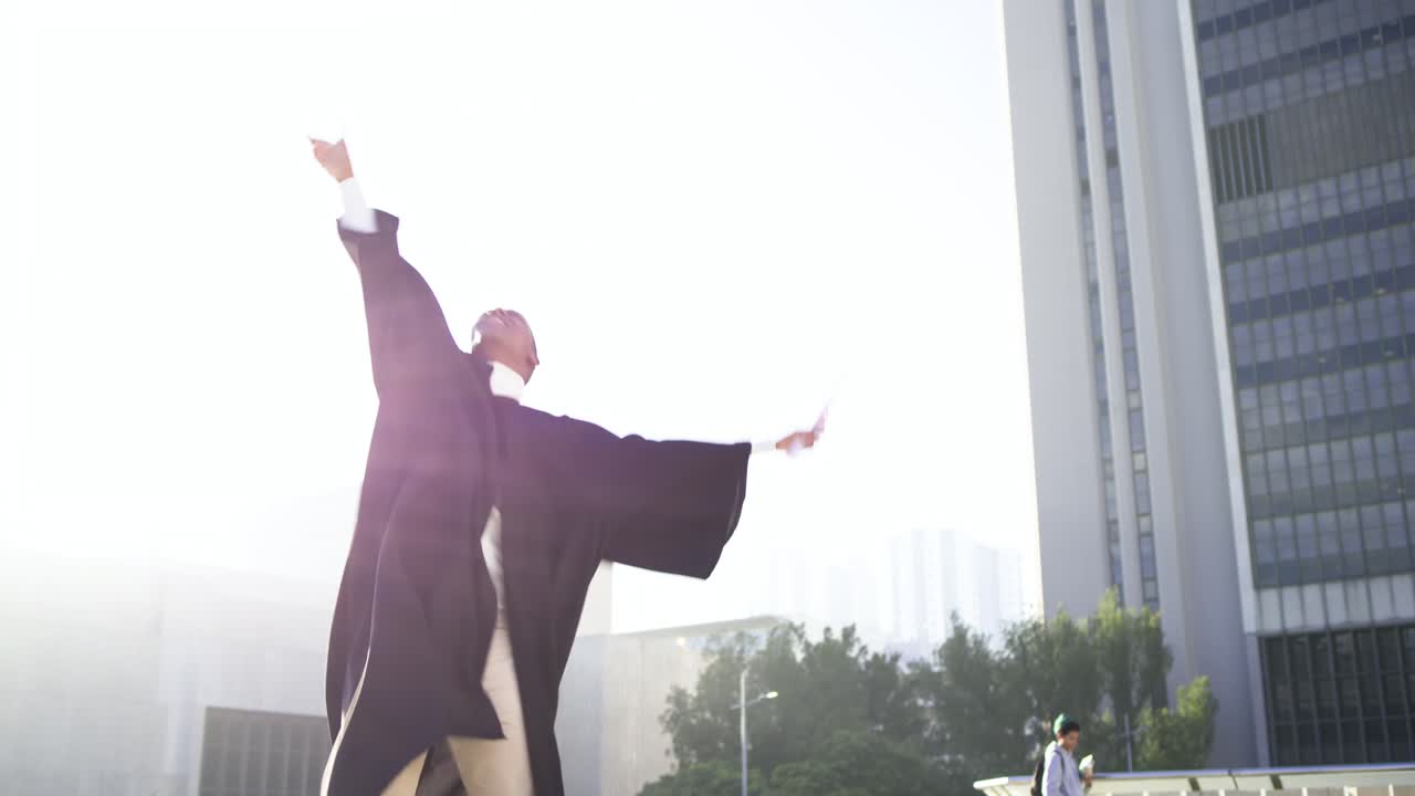 African American male graduate raising scroll, removing cap, tossing cap skyward on rooftop plaza