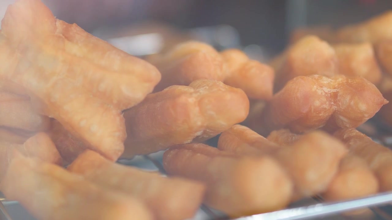 Primo piano di tradizionali bastoncini di pasta fritta asiatici che riposano su una griglia metallica dietro un vetro.