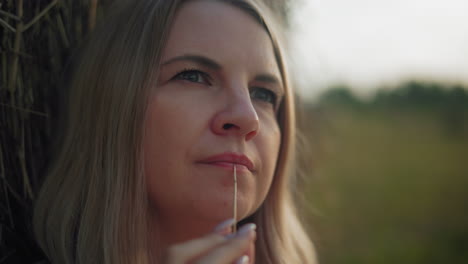 close-up of business woman lost in thought, gently holding a dry stick near her lips, her eyes reflect deep contemplation, set against a softly blurred countryside background