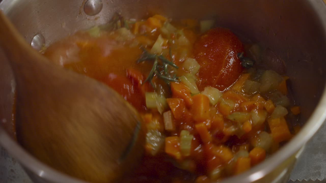 mezcla de verduras hirviendo ztirring de tomates, zanahorias, apio y hierbas dentro de la olla con una cuchara de madera