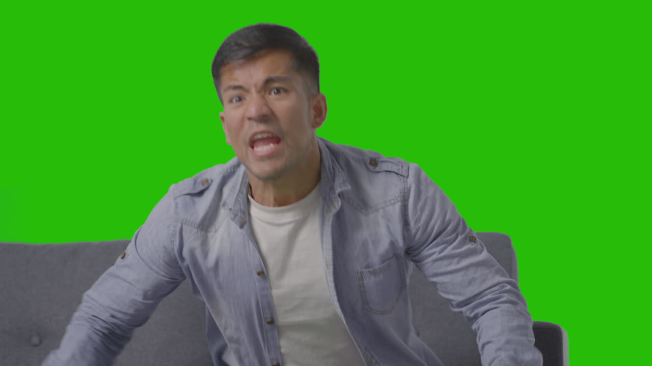 녹색 화면을 배경으로 소파에 앉아 tv로 스포츠를 보는 것을 축하하는 젊은 남자의 스튜디오 샷