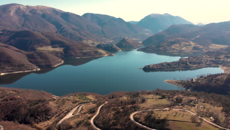 winding road near the calm lake by the mountains in italy. - aerial drone shot