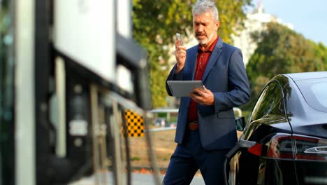 businessman using digital tablet while talking on mobile phone at charging station 4k