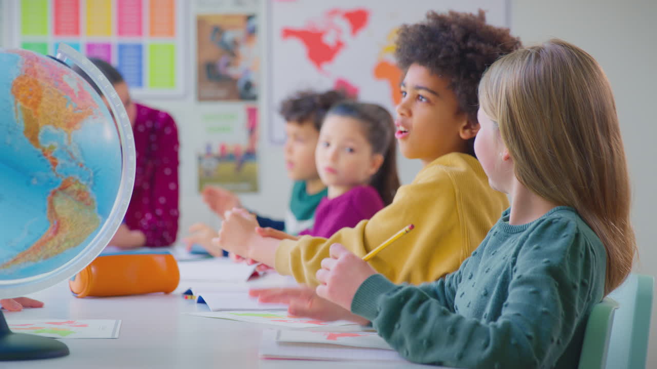 Group Of Multi-Cultural Students Putting Hands Up To Answer Question In Classroom Lesson