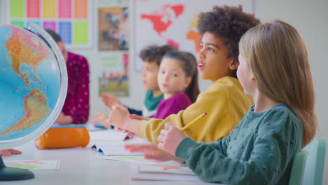 group of multi-cultural students putting hands up to answer question in classroom lesson