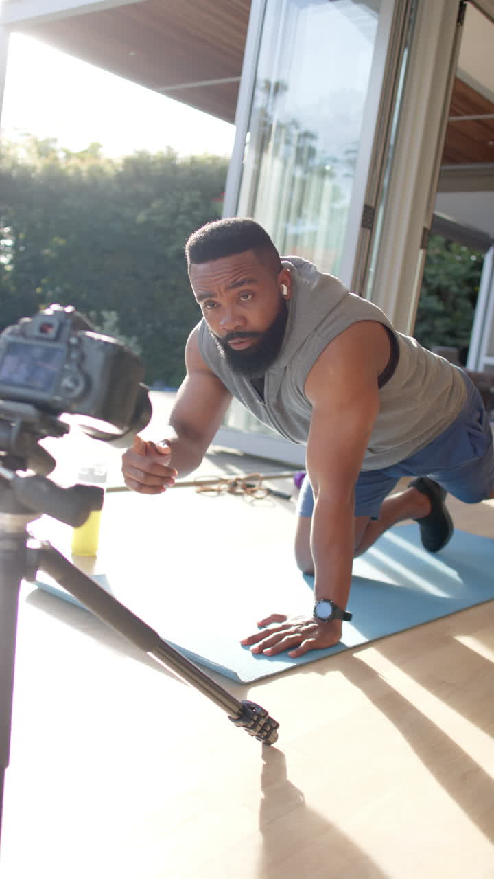 Vertical video of african american male fitness vlogger exercising and filming at home, slow motion