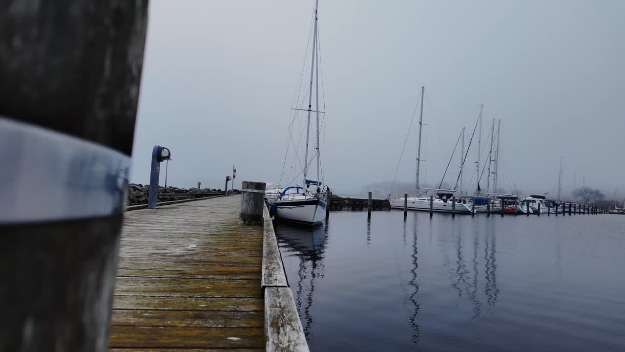 In slow motion, yachts are moored to a wooden pier on a foggy day. Denmark Scandinavia.