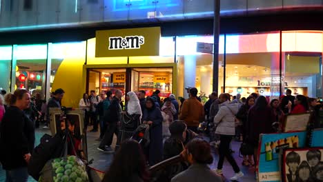 busy evening scene in leicester square with tourists outside m and m's store and a street artist drawing, london