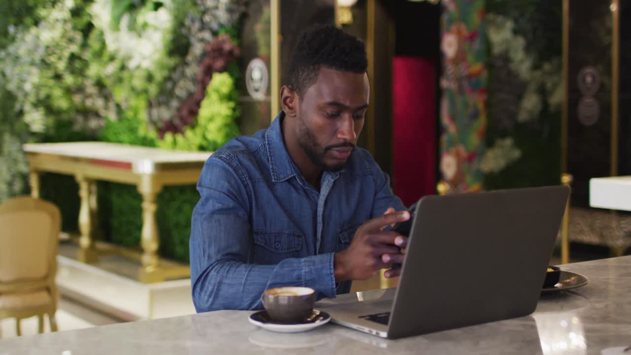 African american businessman using laptop and smartphone in cafe