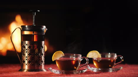 a teapot and two glass cups with tea stand on a table against the background of the fireplace where