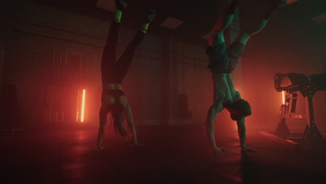 A-man-and-a-woman-do-a-handstand-in-the-gym-together-in-slow-motion.-A-strong-man-and-a-woman-in-a-handstand-walk-across-the-gym-floor-in-colored-oil-lamps