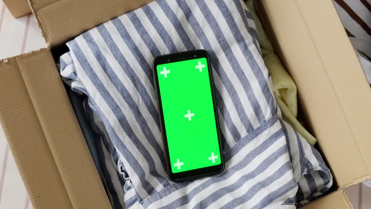 vista superior de la maqueta de pantalla verde del teléfono en una caja con ropa usada.