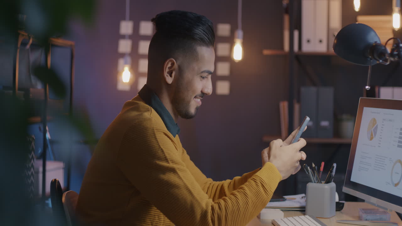 Man working on computer and smartphone in office at night