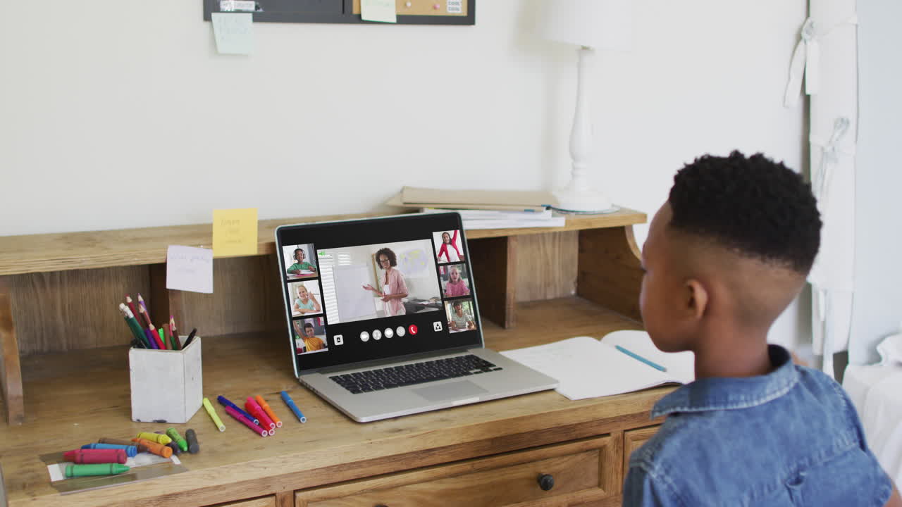 Schoolboy using laptop raising hand in online lesson, with diverse teacher and class screen