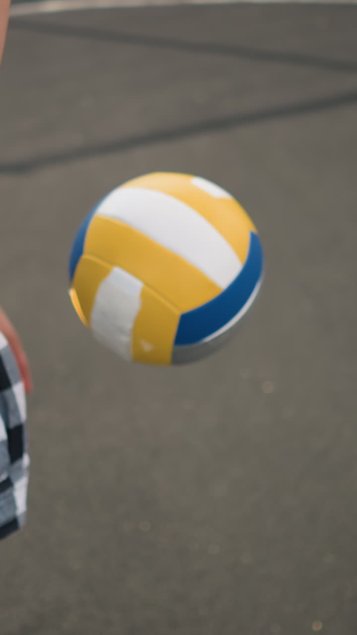 야외에서 공과 손에 초점을 맞추고 볼리볼을 뛰고 있는 허리를 둘러싼 카레드 셔츠를 입은 사람의 측면 뷰의 클로즈업