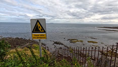 caution sign near rocky seaside in crail