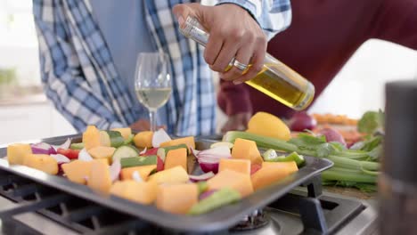 midsection of african american gay male couple pouring olive oil on vegetables, slow motion