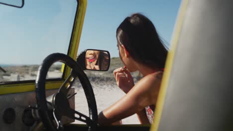 Happy-caucasian-woman-sitting-in-beach-buggy-by-the-sea-doing-make-up