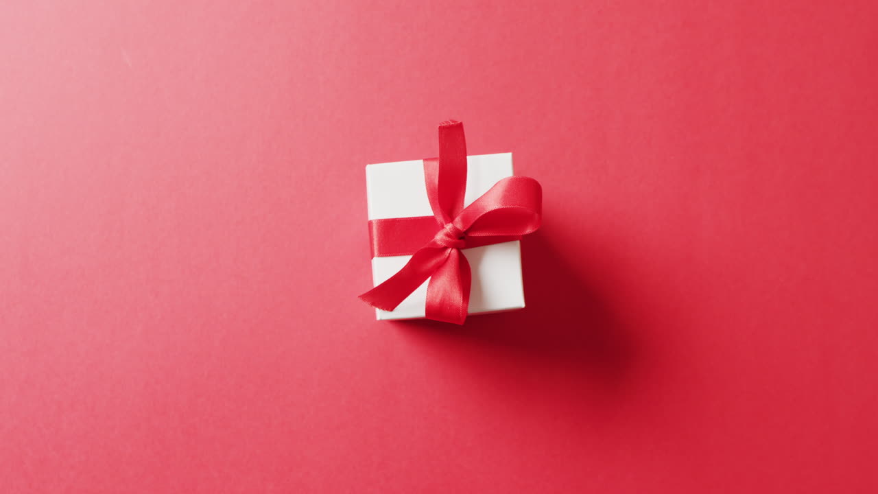 video de arriba de una caja de regalo blanca atada con un lazo rojo, sobre un fondo rojo con espacio de copia