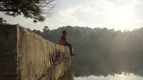 boy seating on a dock on a lake in sunrise moring boy-man water lake