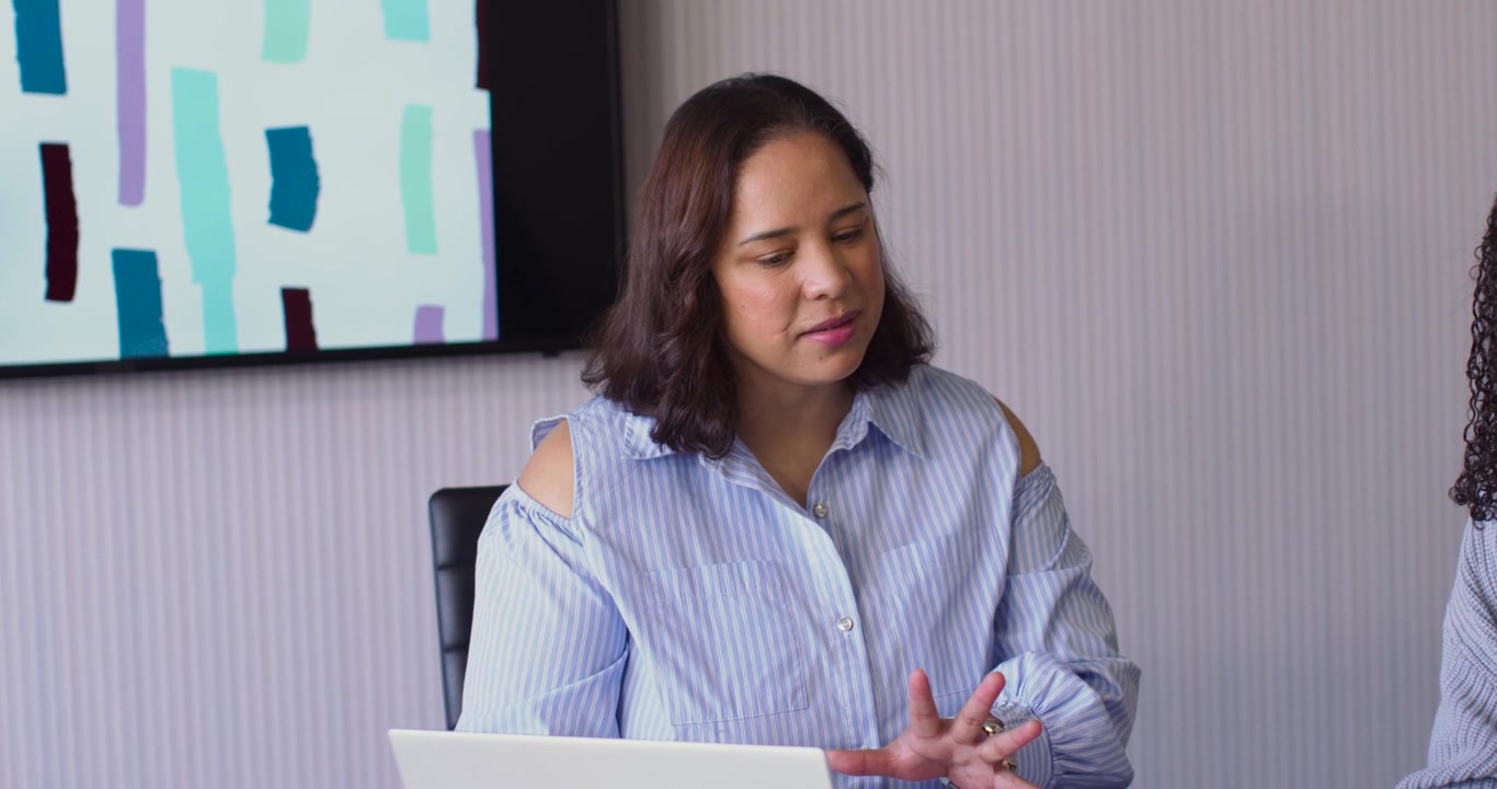 African woman in striped top replying to coworker cue, gesturing and counting at office with laptop