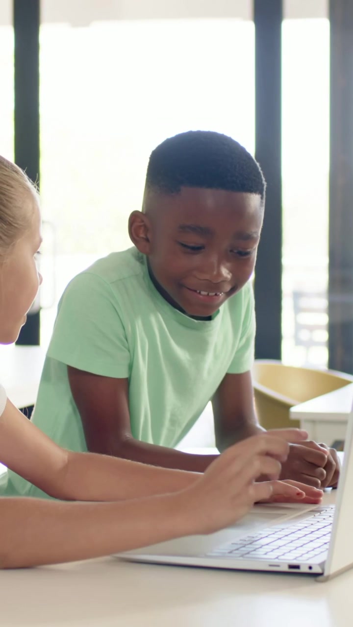 Vertical video: Leaning boy in shirt watching laptop with girl starting typing in class, following