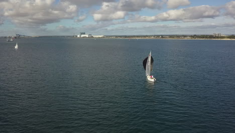 orbiting aerial black spinnaker propels sailboat downwind near