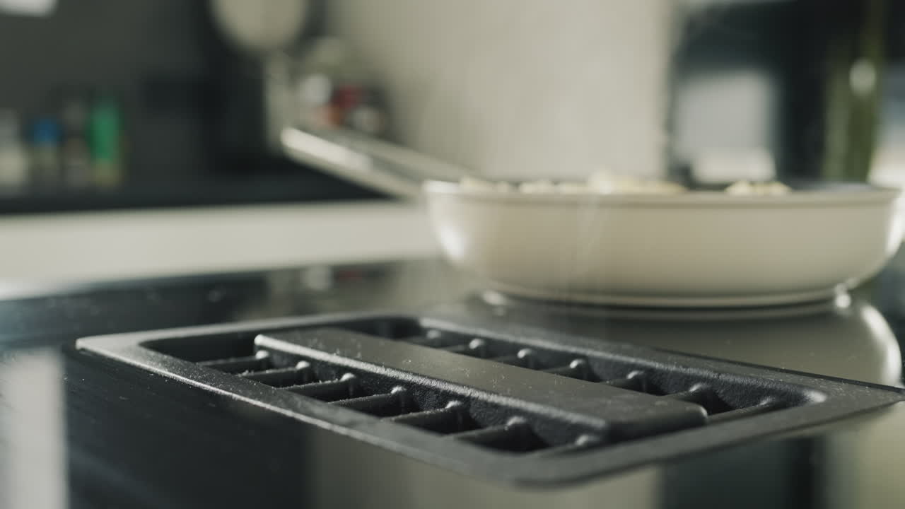 Aardappels worden gebakken op een moderne inductiekookplaat. Ingebouwde afzuigkap werkt. Zijaanzicht.