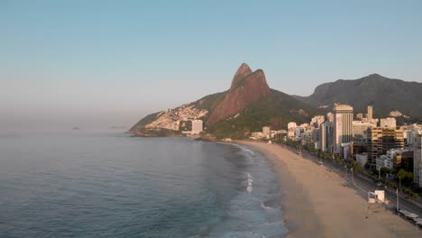 forwards and upwards aerial view of deserted coastal city beach of rio de janeiro during early morning golden hour