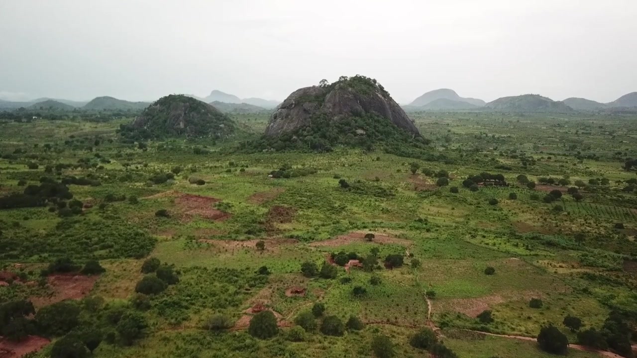 Veduta aerea di terreni agricoli verdi e insediamenti rurali sparsi sotto distintivi inselberg rocciosi nel Mozambico settentrionale