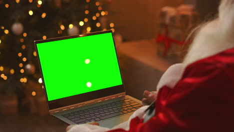 Papá-Noel-Está-Hablando-En-Una-Videollamada-A-Través-De-Una-Computadora-Portátil.-Utilice-La-Pantalla-Verde-Para-Una-Videollamada.-Papá-Noel-Saluda-Con-La-Mano-Mirando-La-Pantalla-Verde-Del-Portátil.-Imágenes-4k-De-Alta-Calidad