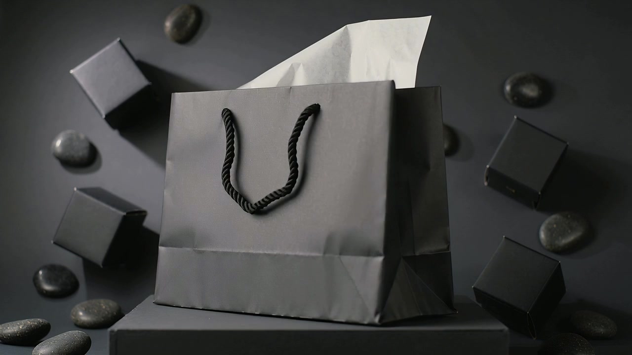 Sacchetto regalo nero rotante con manici intrecciati e carta velina su piedistallo in studio, con scatole in mostra