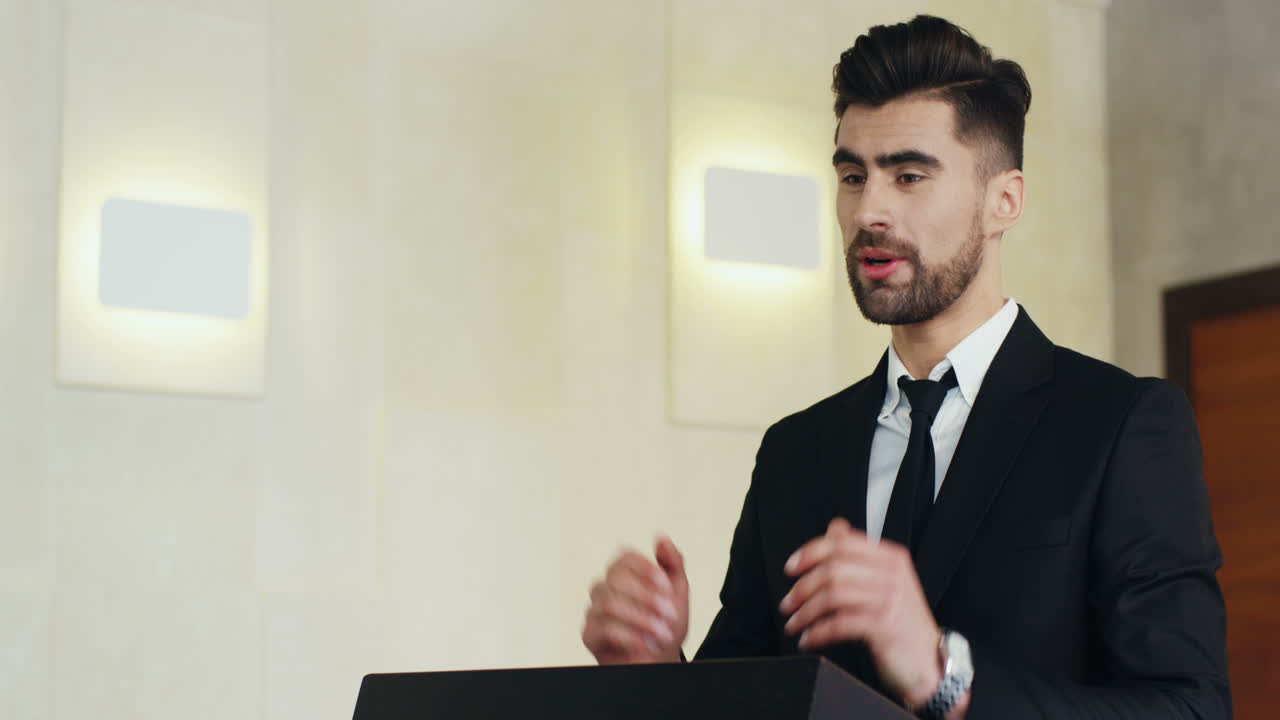 vista de cerca del orador de un hombre de negocios barbudo caucásico en un podio usando ropa formal y hablando en una sala de conferencias