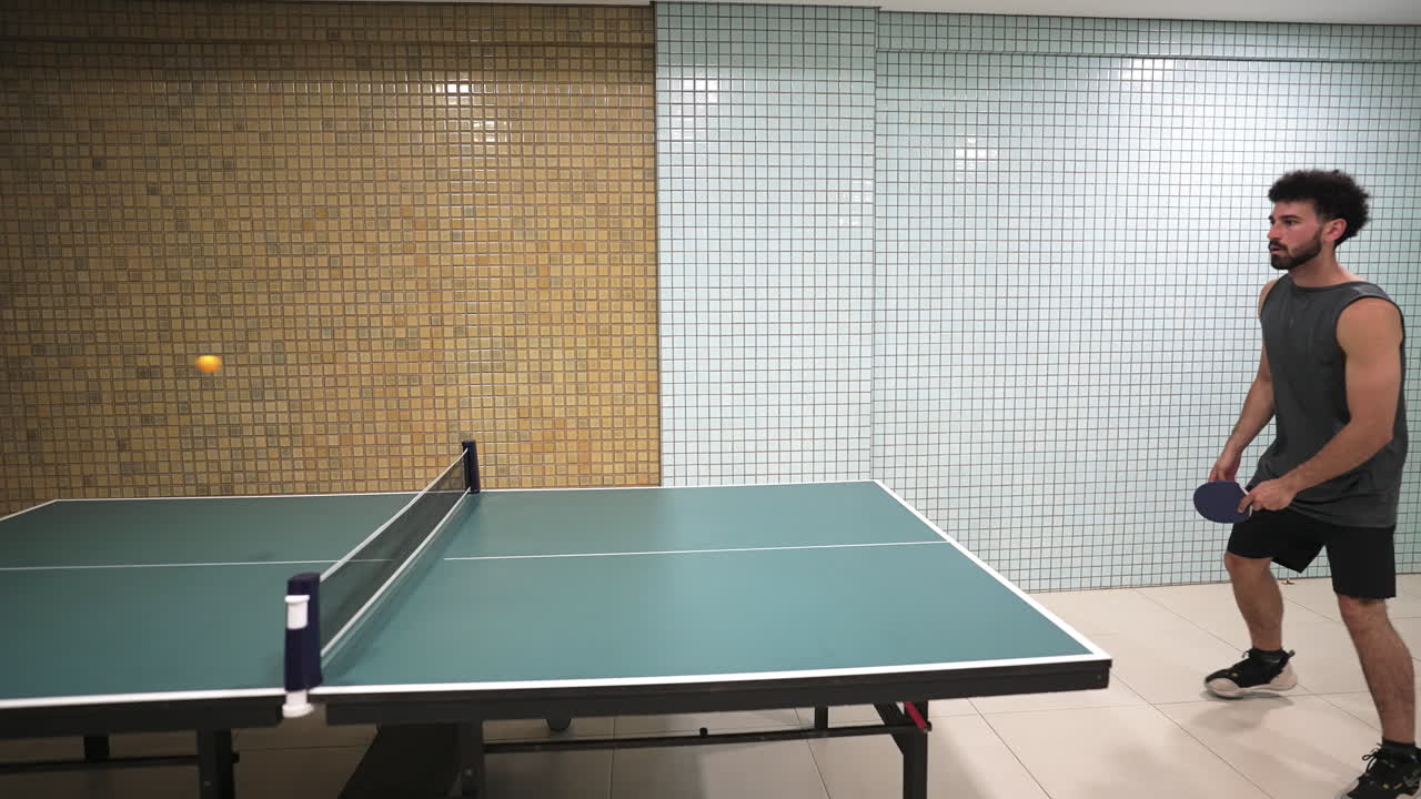 Joven concentrado en golpear la pelota de ping pong con la pala, mostrando una técnica precisa y una gran concentración durante un partido de tenis de mesa competitivo.