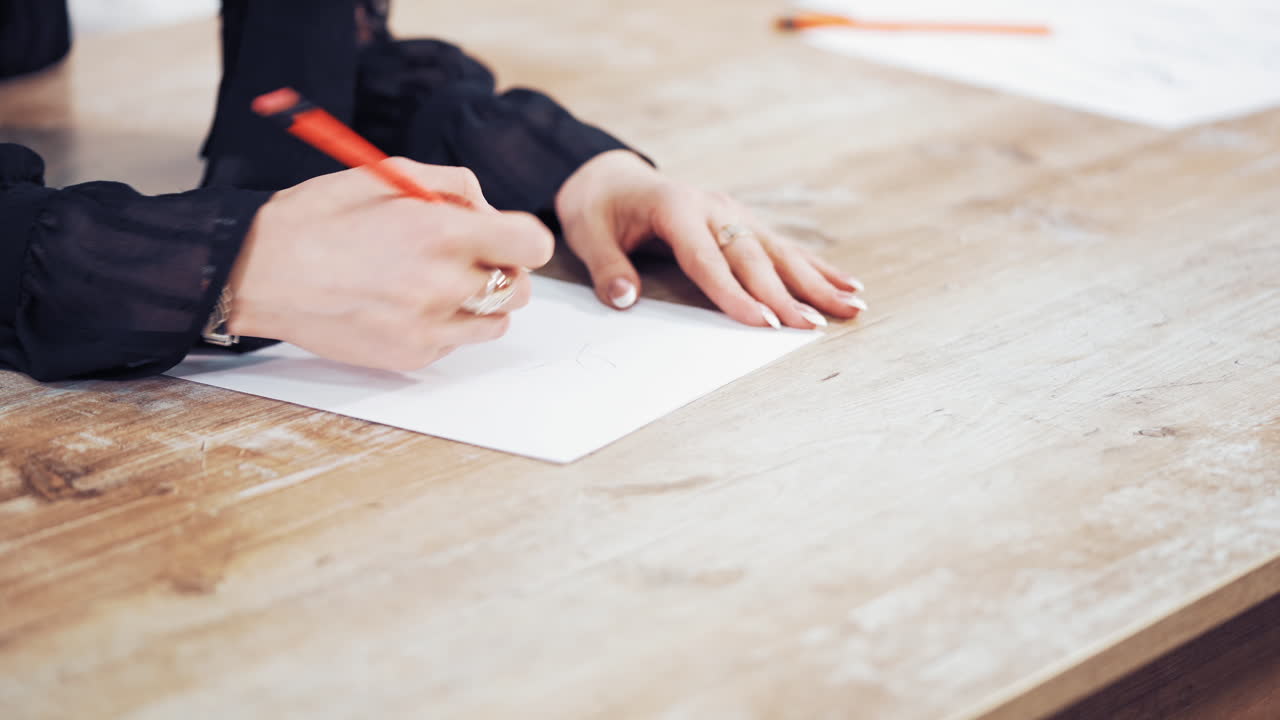 Seamstress draws a sketch of a stylish dress on the wooden background. Woman's hands are making a pattern of a future clothing with a pencil in atelier. Feminine hobby.