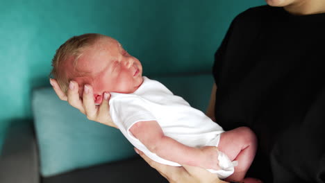 newborn in white bodysuit is slowly waking up. dad's hand tickling baby's belly. close up.