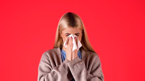 Blonde-woman-sneezes-into-napkin,-bad-feeling,-isolated-red-background,-studio