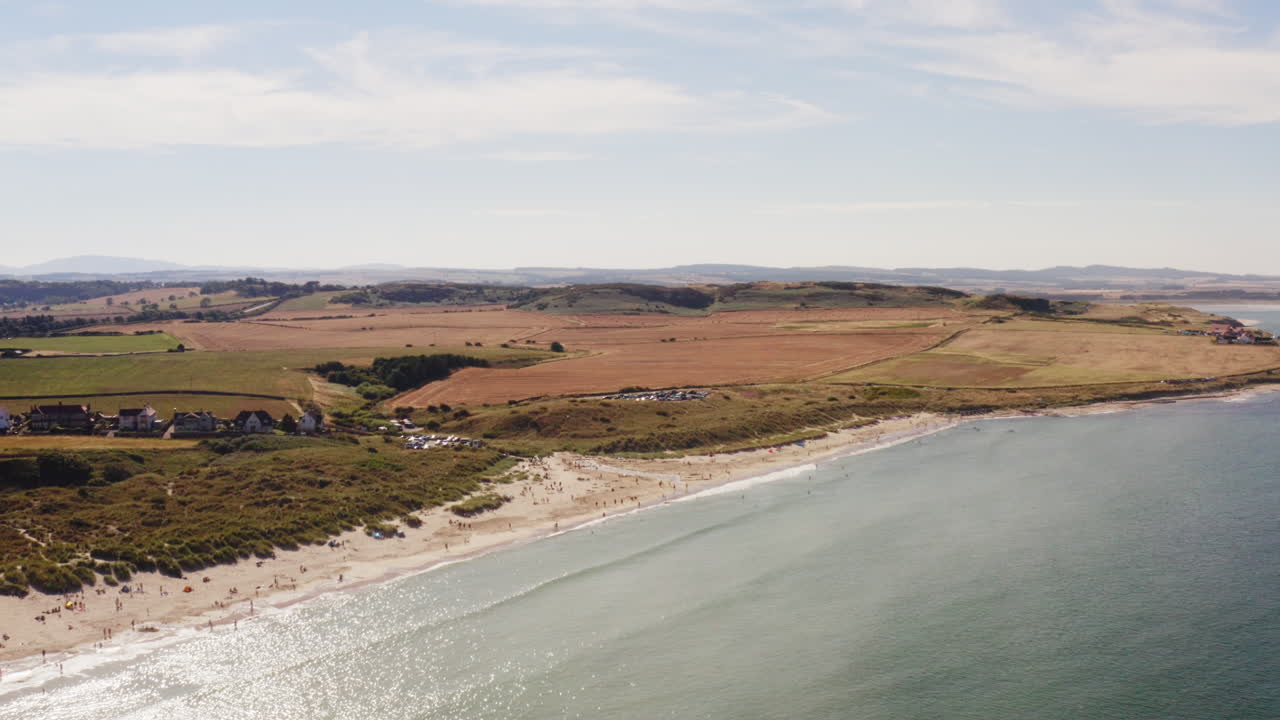 toma aérea de una playa británica en verano, los turistas se relajan y disfrutan de la tranquila playa rodeada de campos verdes