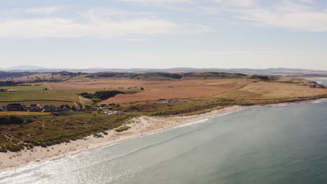 aerial shot of a british beach in the summertime, holidaymakers relax and enjoy the quiet beach surrounded by green fields