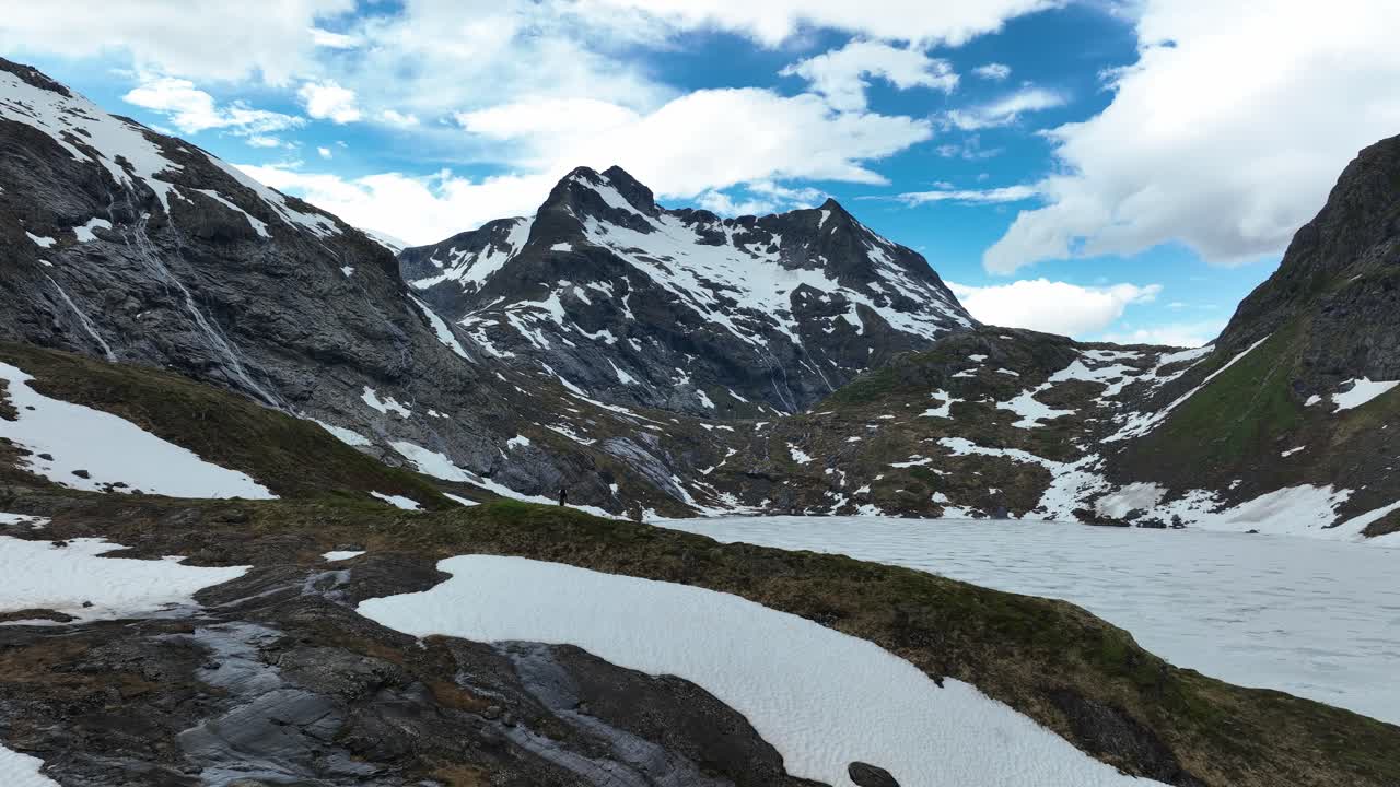 Couple hiking in Norway's Blavatnet, scenic snowy mountains and bright blue sky