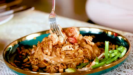 levantando camarones con el tenedor de un plato de pad thai