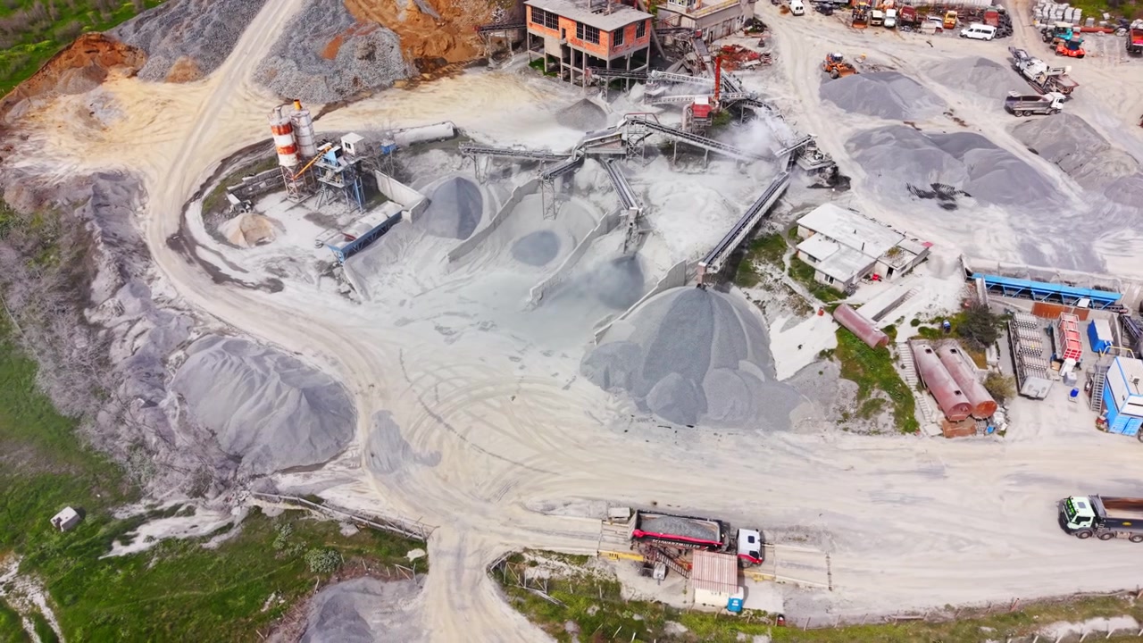 High angle perspective of industrial facility with silos, conveyors, and stockpiles next to a rural road. Aerial view of asphalt concrete plant, Bulgaria.