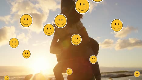 animación de iconos emoji sobre una feliz pareja afroamericana abrazándose en la playa