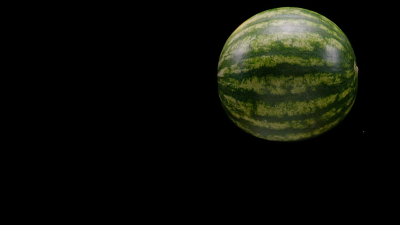sandía cayendo y girando aislada en fondo negro, cámara lenta