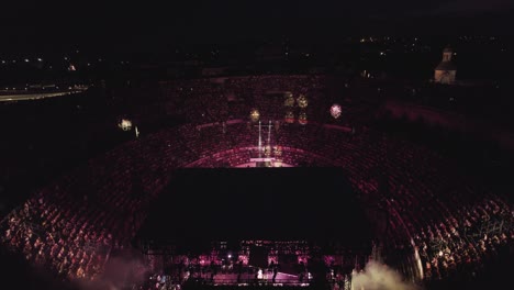 Drone-to-lend-in-the-Arenas-de-Nîmes-in-the-middle-of-the-night,-people-are-watching-the-concert-and-there-are-lights-of-several-colors