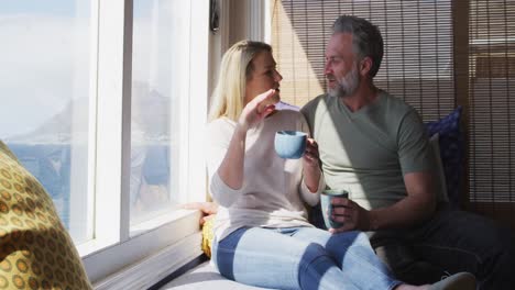 Entspannendes-Kaukasisches-Reifes-Paar,-Das-Kaffee-Trinkt-Und-Sich-Im-Sonnigen-Wohnzimmer-Unterhält